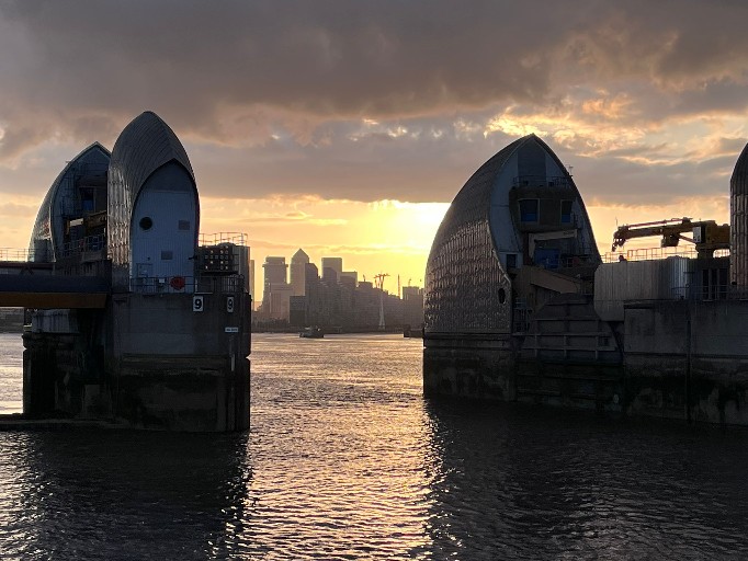 Looking through the Thames Barrier piers at sunset with Canary Wharf visible in the distance